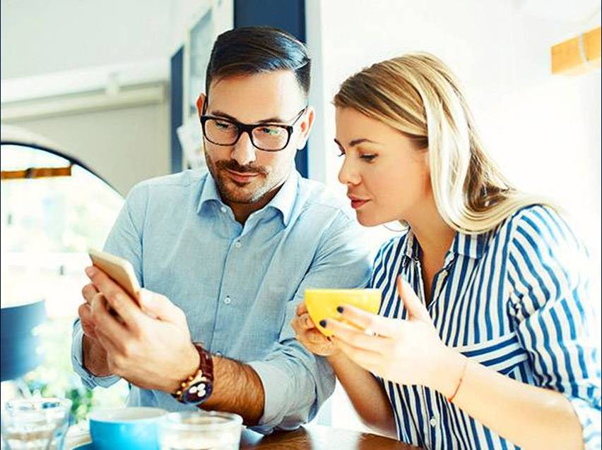 Ζευγάρι ελέγχει κινητό τηλέφωνο και πίνει καφέ.